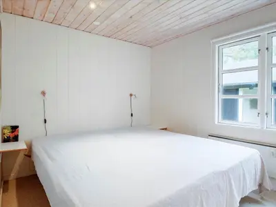 a white bedroom with a bed and a window at Holiday Home Patti - 700m from the sea by Interhome in Blokhus