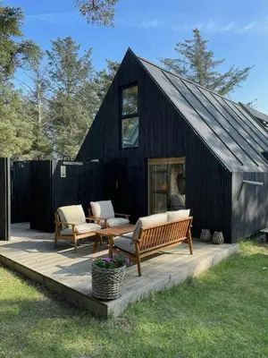 a black house with two chairs and a bench on a deck at Cosy Little Wooden House On Natural Grounds in Vestervig