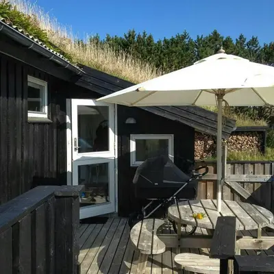 a patio with an umbrella and a stroller on a deck at Holiday Home By The North Sea Dunes In Rødhus in Pandrup