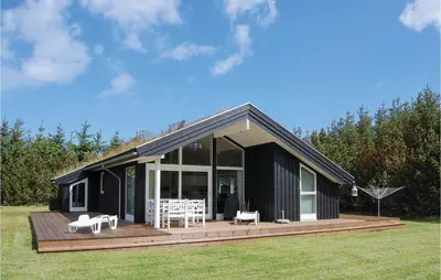 a black house with a wooden deck in a field at Holiday Home Pandrup 07 in Pandrup