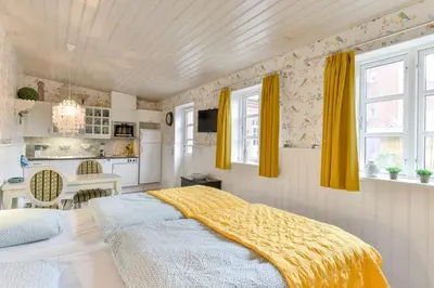 a bedroom with a bed and a kitchen with yellow curtains at Viborg City Rooms in Viborg