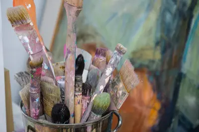 a cup full of paint brushes in front of a painting at Kunstart20 in Saltum