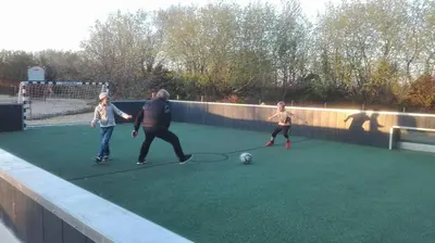 three people playing with a soccer ball on a artificial field at Myrhoj Camping in Myrhøj