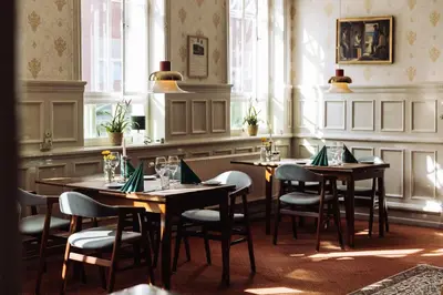 a dining room with tables and chairs and windows at Hotel Lidenlund in Lemvig
