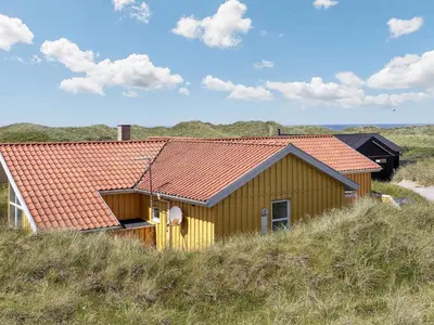 a yellow house with an orange roof on a hill at 10 person holiday home in Løkken in Løkken