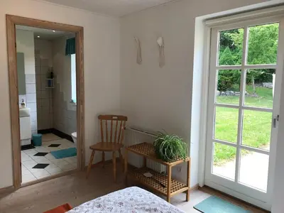 a bedroom with a table and a chair and a bathroom at Tranum Lys og Glas in Brovst