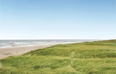 a beach with green grass and the ocean at Three-Bedroom Holiday Home In Harboore in Harboør