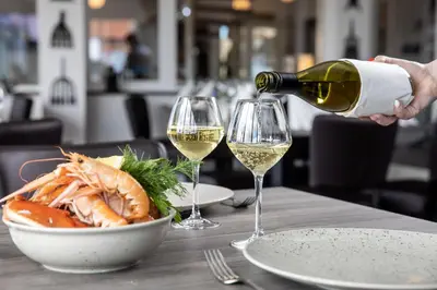a person pouring white wine into two wine glasses at Thyborøn Hotel in Thyborøn