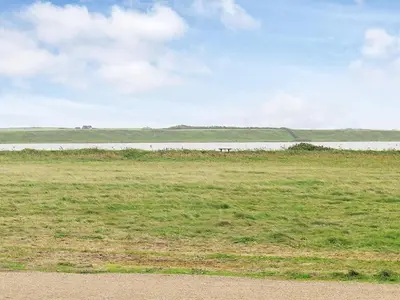 a field of grass with a body of water in the background at 8 person holiday home in Harboøre in Harboør