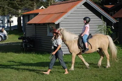 a young girl riding on a horse with a woman at Hytteby – Hanstholm Camping – Thy Feriepark in Hanstholm