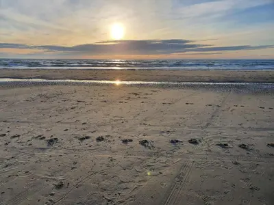a beach with the sun setting over the ocean at Seaside Serenity in Blokhus-By Traum in Blokhus