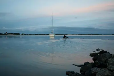 a person sitting on a boat in the water with a sailboat at Tambohus Kro & Badehotel in Hvidbjerg