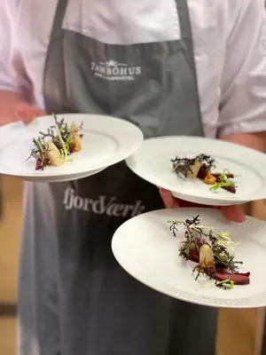 a chef is holding three plates of food at Tambohus Kro & Badehotel in Hvidbjerg