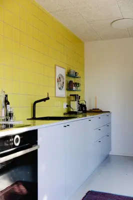 a kitchen with white cabinets and a yellow wall at Containerhus 18b in Harboør
