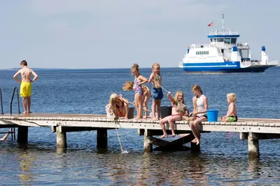 a group of children sitting on a dock in the water at Hvalpsund Færgekro in Hvalpsund
