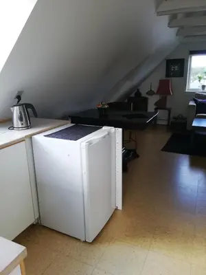 a white refrigerator in a living room with a table at Hunetorpvej Holiday Apartment in Blokhus