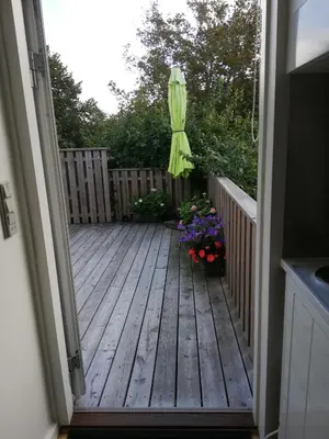 an open door to a deck with flowers and an umbrella at Hunetorpvej Holiday Apartment in Blokhus