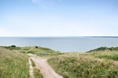 a dirt road on a grassy hill next to the ocean at Thatched Holiday Home in Struer, Jutland with a view in Struer
