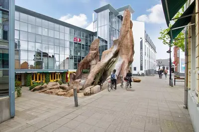two people riding bikes down a street with a sculpture at Marieshus in Holstebro