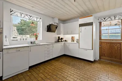 a kitchen with white cabinets and a large window at Logi i hus med kunst og have in Vestervig