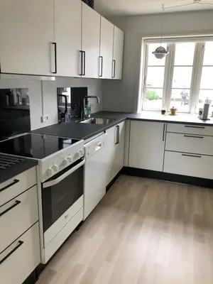 a kitchen with white cabinets and a wooden floor at BrusaaUdlejning in Nibe