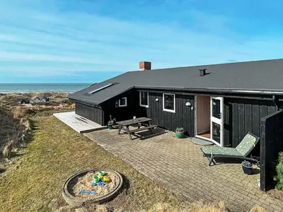 a black house with a picnic table and a bench at 6 person holiday home in Løkken in Løkken
