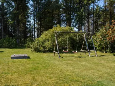 an empty swing set in a park with a grass field at 6 person holiday home in Løkken in Løkken