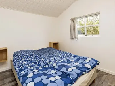 a bedroom with a bed with a blue comforter and a window at Cozy Coastal Retreat in Gronhoj-By Traum in Løkken