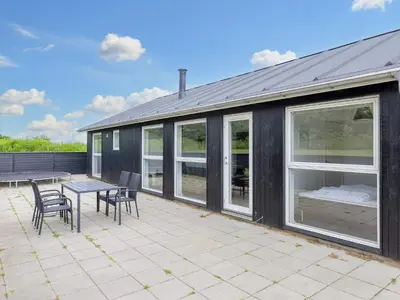 a black house with a table and chairs on a patio at 6 person holiday home in Løkken in Løkken