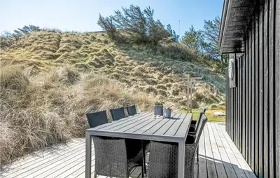 a table and chairs on a deck with a hill at Holiday Home Tobaksvej in Blokhus