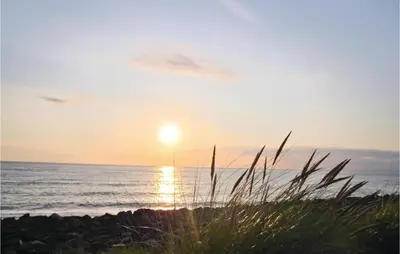 a sunset on the beach with the ocean and grass at Holiday Home Kjeldbjergvej Lemvig Iii in Lemvig