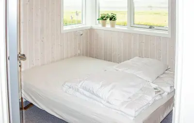 an unmade bed in a room with two windows at Holiday Home Houmøllevej in Karby
