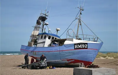 a boat on the beach with two men standing next to it at Holiday Home N C Alstedsvej Fjerritslev Xii in Fjerritslev