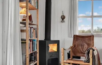 a fireplace in a living room with a chair and a bookcase at Holiday Home Svenstibakkevej Denmark in Frøstrup