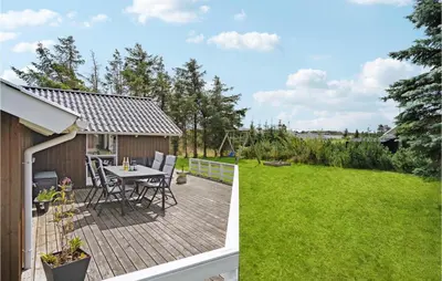 a wooden deck with a table and chairs on a lawn at Holiday Home Kristavej Løkken Xii in Løkken