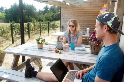 a man and a woman sitting at a picnic table with a laptop at Stone Mountain BnB in Stenbjerg