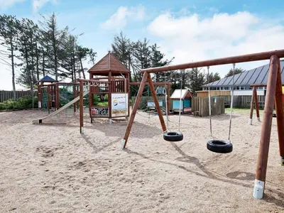 a playground with a swing set in the sand at 4 person apartment in holiday park Blokhus in Blokhus