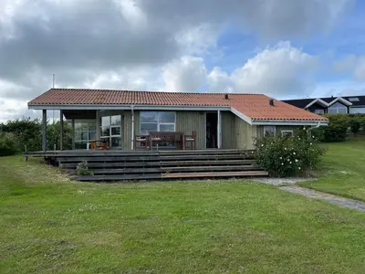 a small green house with a table on the porch at Ældre Sommerhus Max 4 voksne og 4 børn in Lemvig