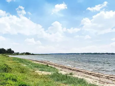 a beach with grass and water on a cloudy day at 6 person holiday home in Farsø-By Traum in Farsø