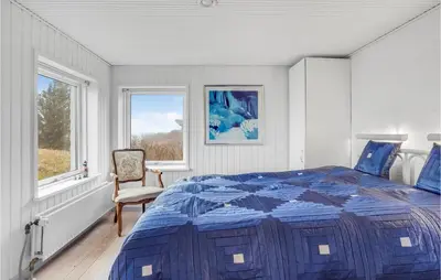 a bedroom with a bed and a chair and windows at Stunning Home In Blokhus in Blokhus