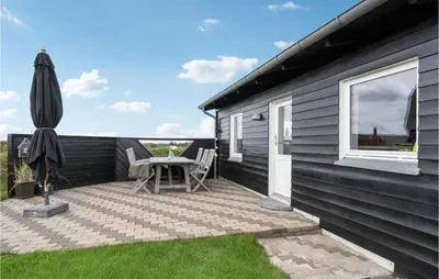 a patio with a table and an umbrella on a house at Stunning Home In Blokhus in Blokhus