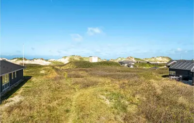 a house on top of a grassy hill with buildings at 3 Bedroom Gorgeous Home In Blokhus in Blokhus