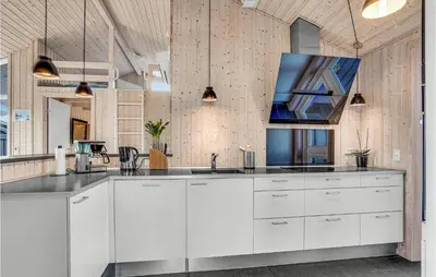 a kitchen with white cabinets and a tv on the wall at Nice Home In Blokhus With Kitchen in Blokhus