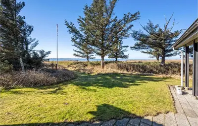 an open yard with trees and the ocean in the background at 3 Bedroom Gorgeous Home In Thyholm in Thyholm