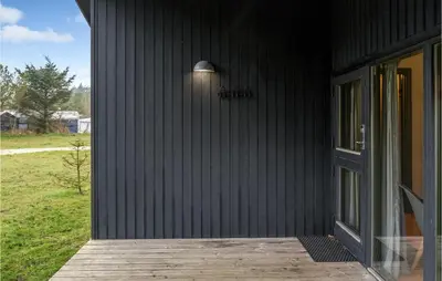 a black house with a wooden porch with a door at Cozy Home In Hanstholm With Kitchen in Hanstholm