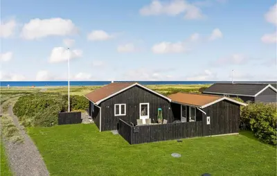 a black house on a lawn with the ocean in the background at Lovely Home In Løgstør With Kitchen in Løgstør