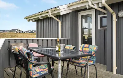 a table with chairs and a bottle of wine on a deck at Cozy Home In Harboøre With Sauna in Harboør