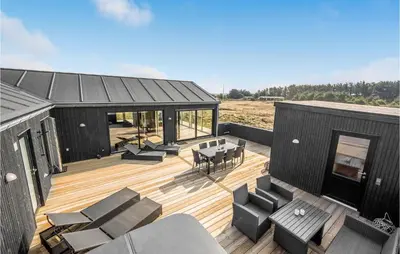 a black house with a deck with a table and chairs at Awesome Home In Harboøre With Kitchen in Harboør