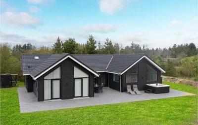 a black cabin with a patio in the grass at Gorgeous Home In Blokhus With Jacuzzi in Blokhus