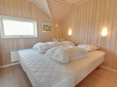 a bedroom with a bed with white sheets and a window at Holiday Home Egidia - 50m from the sea by Interhome in Lemvig